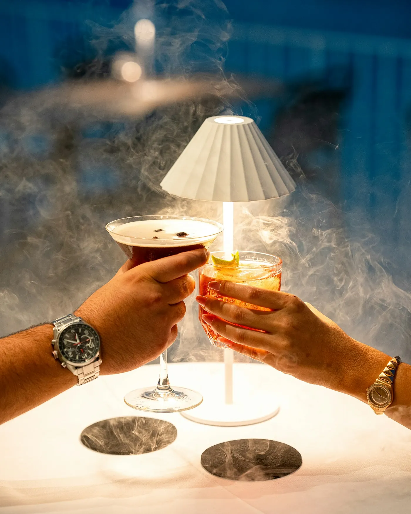 Two guests raising cocktails across a softly lit table
